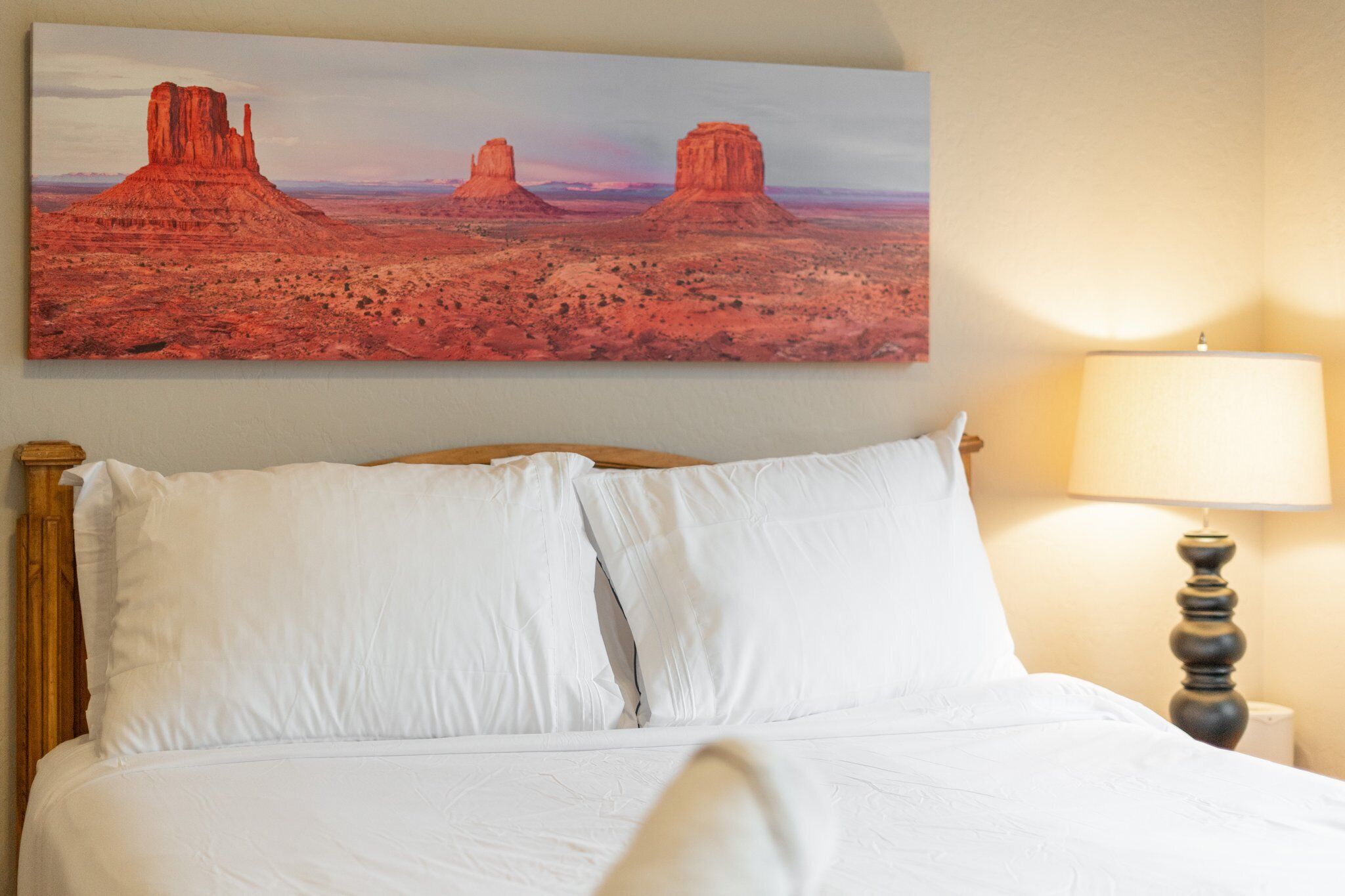 Ein Bett mit weißer Bettwäsche, ein Holz-Kopfteil und ein Gemälde von roten Felsformationen an der Wand darüber.