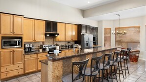 A modern kitchen with wooden cabinets, granite countertops, a central island with bar stools, stainless steel appliances, and a chandelier. - Luxury 5 Bedroom Scottsdale Home with Heated Pool! (Scottsdale)