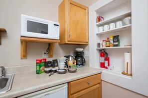 Una kitchenette compacta con microondas, cafetera y varios utensilios de cocina en la encimera.