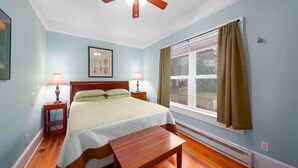 A bedroom with a bed, two bedside lamps, a ceiling fan, a window with curtains, and a framed picture on the wall. - Private Suite Walk Downtown- Private Bath-Private entrance. (Asheville)