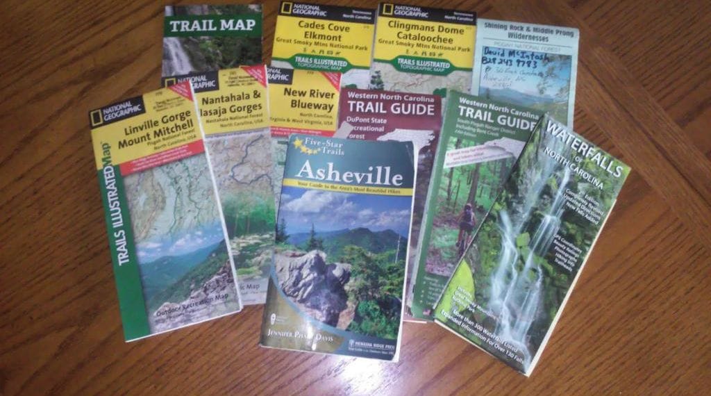 A collection of trail maps and guides on a wooden surface.