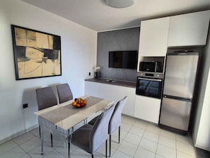 A modern kitchen with a dining area, a flat-screen TV, a built-in oven, and a stainless steel refrigerator. - Holiday flat with sea view (Njivice)