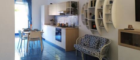 A modern kitchen with a dining area, a sofa, and a unique wall shelf unit.