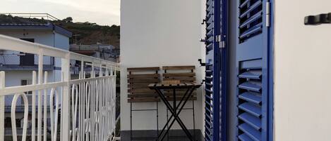 A balcony with a white railing, a table with chairs, and blue shutters.
