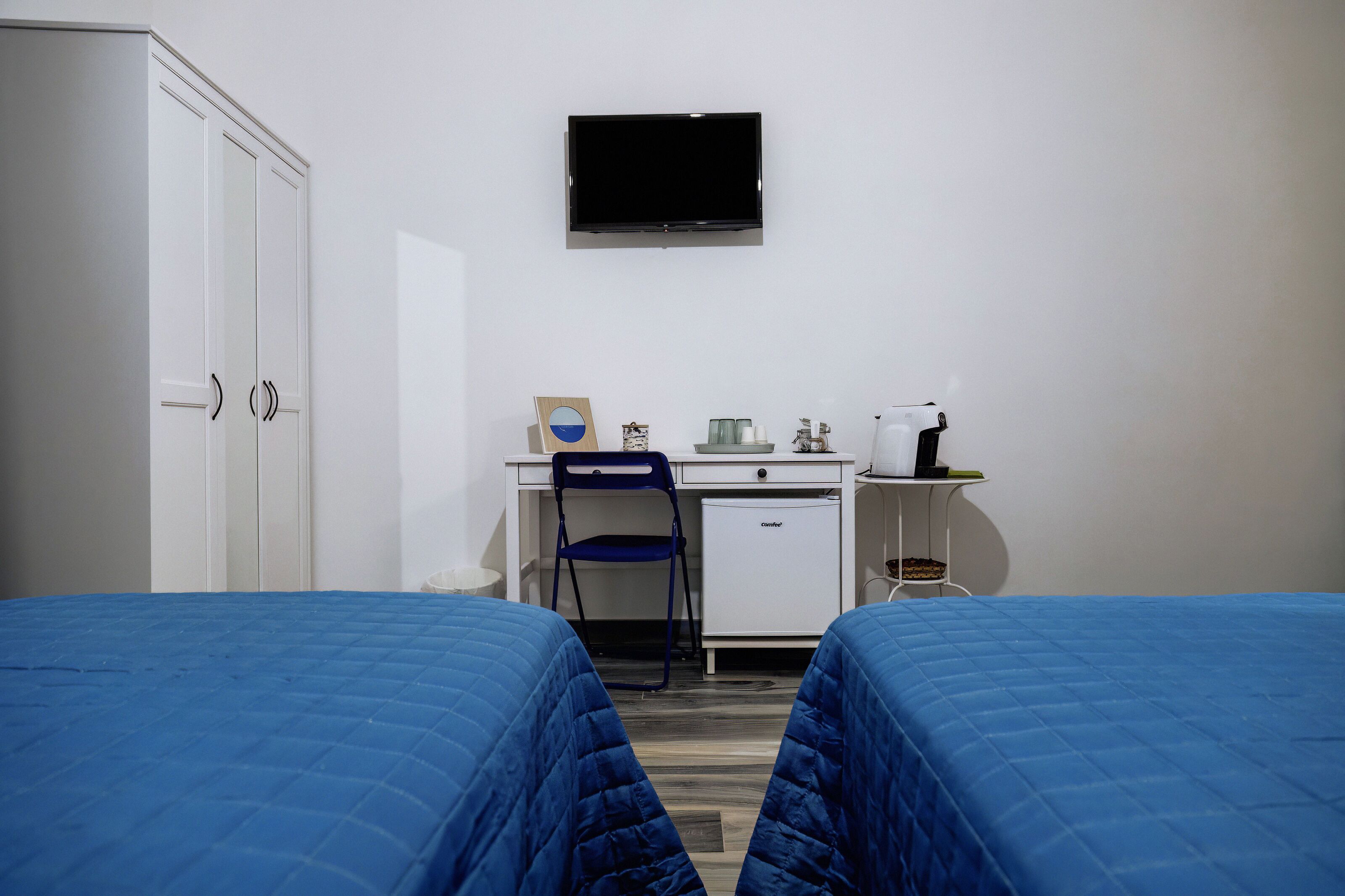 A hotel room with two beds, a desk, a chair, a television, and a mini-fridge.