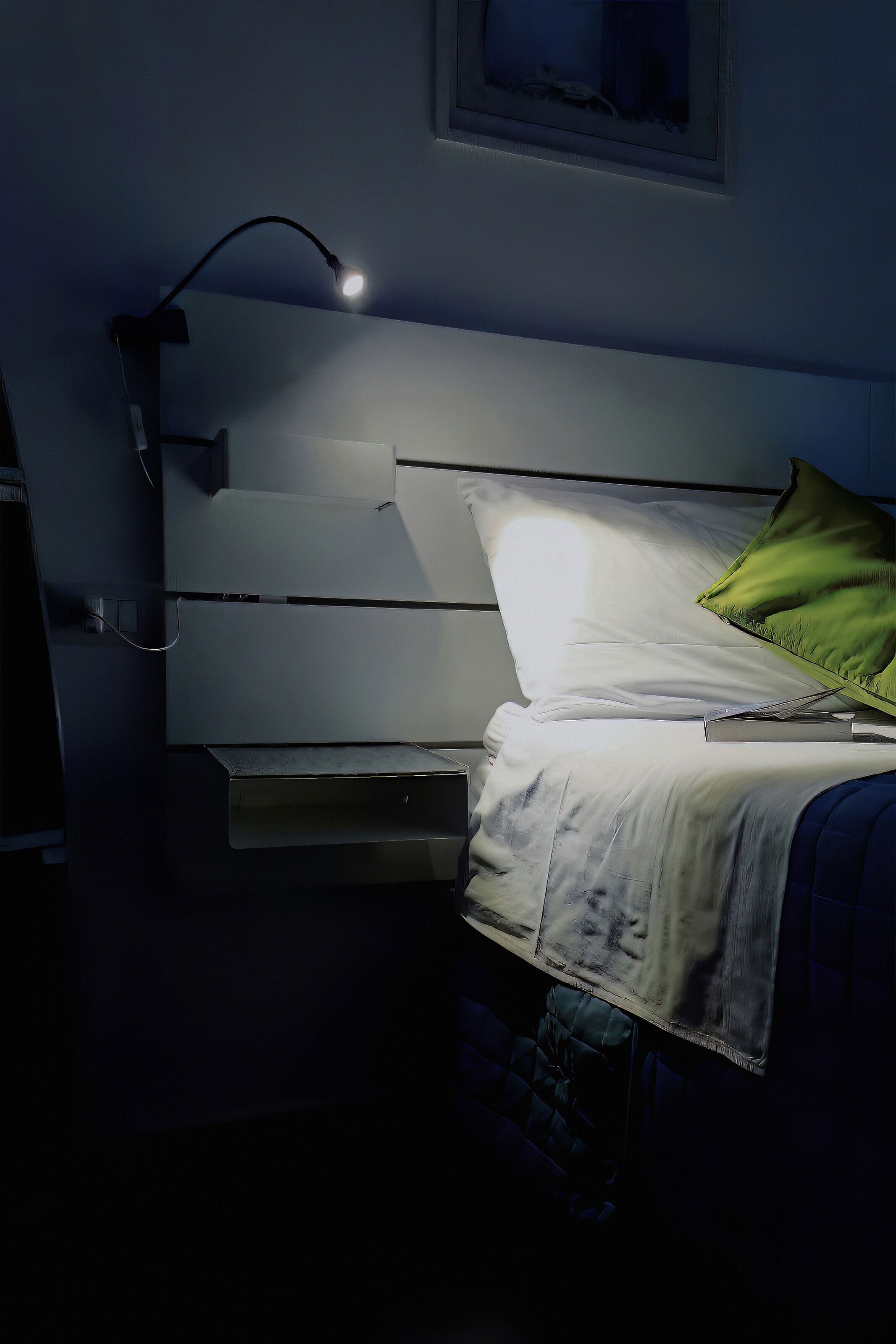 Una cama con cabecera blanca, almohada verde y una lámpara de noche.