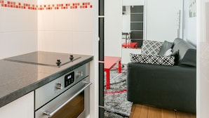A compact kitchen with modern appliances, a dining area with a red table, and a living space with a black sofa. - Sourdière Opéra Louvre Vendôme (Paris)