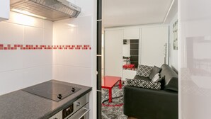 A compact kitchen with a built-in stove, a red table, and a black sofa in the adjacent living area. - Sourdière Opéra Louvre Vendôme (Paris)