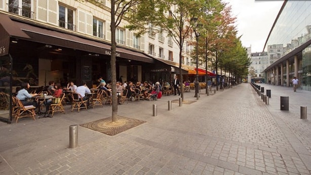 An outdoor café with tables and chairs, a cobblestone pathway, and buildings in the background. - Sourdière Opéra Louvre Vendôme (Paris)