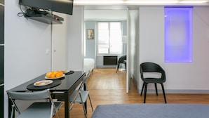 A modern room with a bed, a desk with a chair, a flat-screen TV mounted on the wall, and a dining table with chairs. - Sourdière Opéra Louvre Vendôme (Paris)