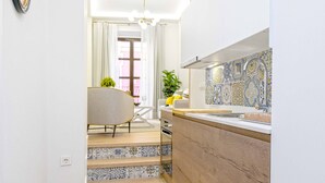 Un pasillo estrecho que conduce a una cocina con salpicadero de azulejos y una zona de comedor con una silla y una mesa.