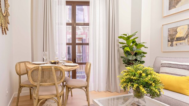 Un comedor con sillas de mimbre, una mesa de vidrio y un jarrón con flores amarillas.