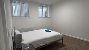 A small, neatly arranged bedroom with a single bed, two windows, a radiator, and a bedside table with a lamp. - Buckie Haven 3 Bed Contractors Business Travellers (Buckie)