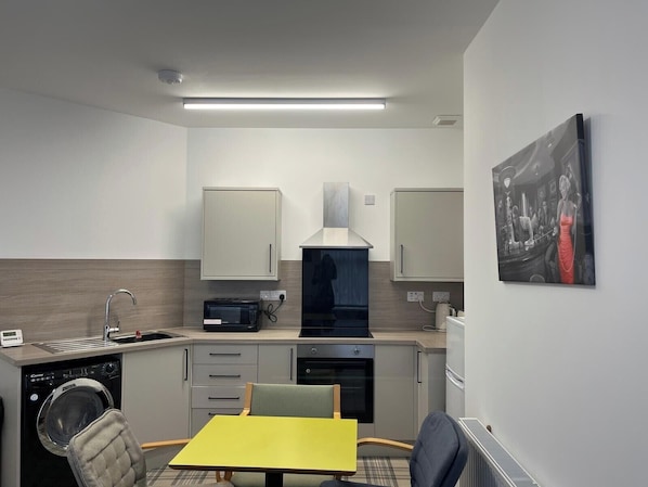 A compact kitchen with a microwave, toaster, and built-in oven. There is a sink with a faucet, a chair, and a table. - Buckie Haven 3 Bed Contractors Business Travellers (Buckie)