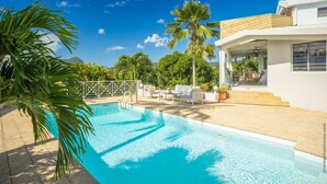 A modern pool area with a clear blue pool, white lounge chairs, and palm trees. - Manguier (Le Diamant)