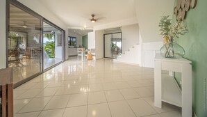 A spacious living area with a large sliding glass door leading to a balcony, a ceiling fan, and a dining area with a table and chairs. - Manguier (Le Diamant)