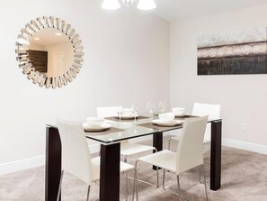 A dining area with a glass table, white chairs, a modern mirror, and a painting on the wall. - Cozy 2 Bed Town Home in Balmoral Resort-2SLTTH2 (Haines City)