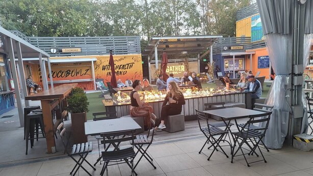 Un café al aire libre con mesas y sillas, una zona de bar con mostrador y un letrero que dice "CocoBowlz".