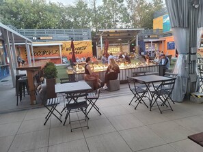 Un café al aire libre con mesas y sillas, una zona de bar con mostrador y un letrero que dice "CocoBowlz".