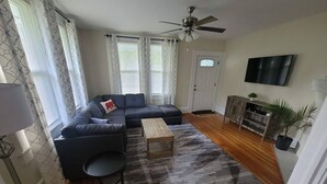 Una sala de estar con un sofá modular, una mesa de centro, un ventilador de techo y un televisor montado en la pared.