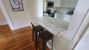 Una cocina con armarios blancos, encimera de mármol y dos taburetes de bar.