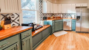 A kitchen with green cabinets, a wooden countertop, a stainless steel refrigerator, and a patterned backsplash. - The Blue Door Bungalow - Central & Walkable to Downtown & Indiana University (Bloomington)