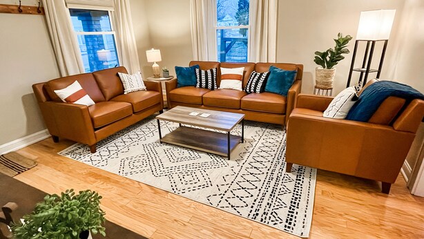 A living room with a brown leather sofa set, a coffee table, and a patterned rug. - The Blue Door Bungalow - Central & Walkable to Downtown & Indiana University (Bloomington)