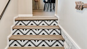 A staircase with patterned steps and a handrail, leading to a dining area with chairs and a table. - The Blue Door Bungalow - Central & Walkable to Downtown & Indiana University (Bloomington)