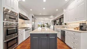 A modern kitchen with white cabinetry, stainless steel appliances, a central island, and a tiled floor. - Overlook Oasis-Stunning Views-Pool and Spa! (Austin)