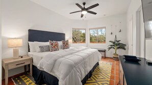 A bedroom with a bed, bedside table, lamp, ceiling fan, windows, and a potted plant. - Overlook Oasis-Stunning Views-Pool and Spa! (Austin)