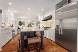 A modern kitchen with white cabinetry, a stainless steel refrigerator, and a central island with bar stools.