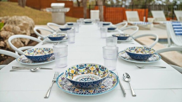 An outdoor dining area with white tables, blue and white patterned bowls, clear glasses, and metal cutlery. - Overlook Oasis-Stunning Views-Pool and Spa! (Austin)