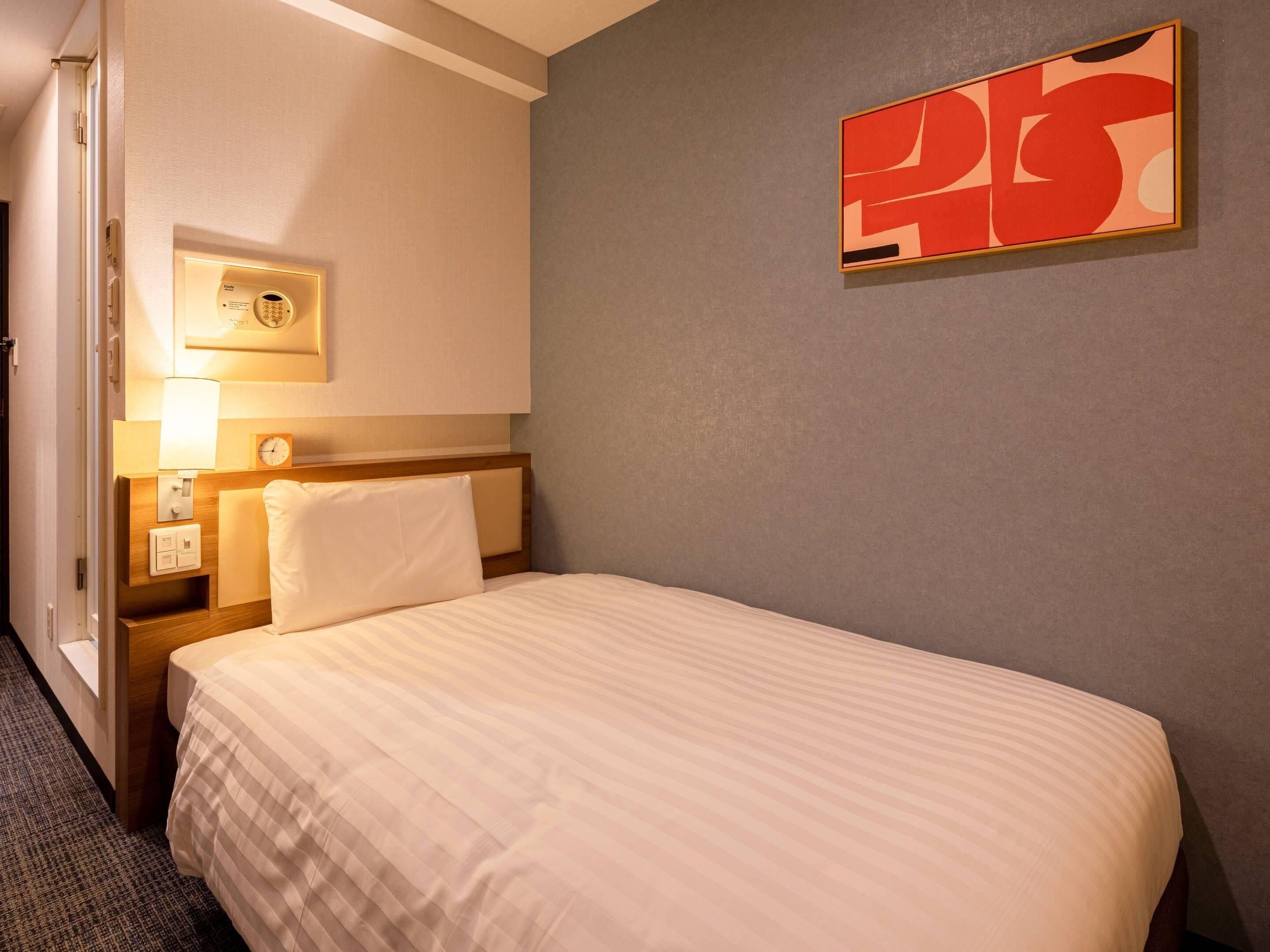 Ein Hotelzimmer mit Bett, Nachttisch mit Lampe, Wanduhr und einem Gemälde.