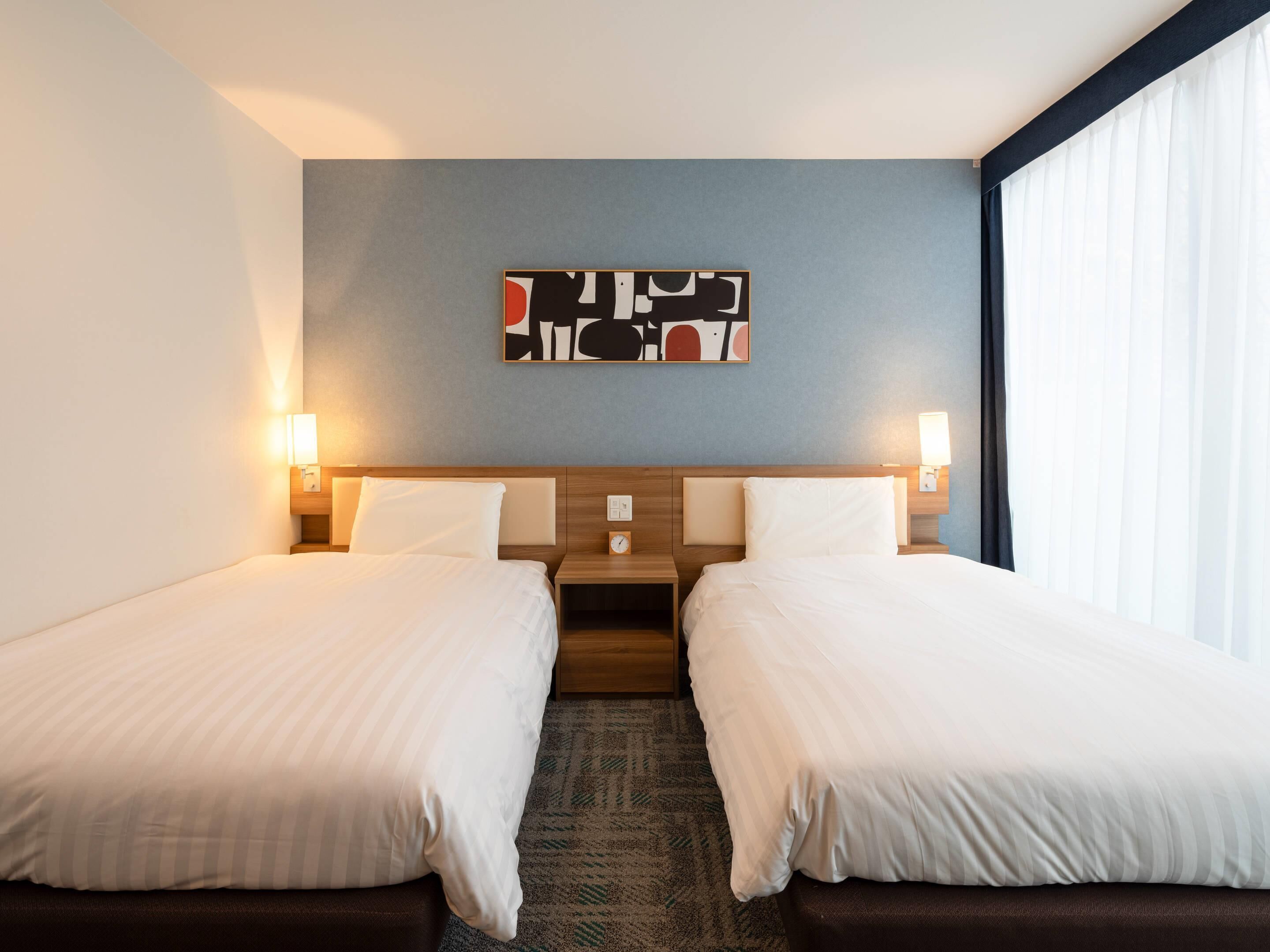 A hotel room with two beds, a modern headboard, a wall-mounted abstract art piece, and a window with curtains.