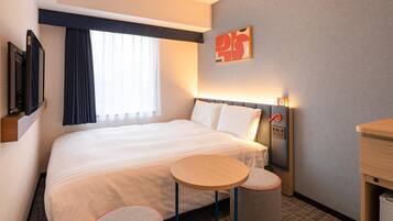 A hotel room with a large bed, a bedside table, two small stools, a TV, and a window with curtains.