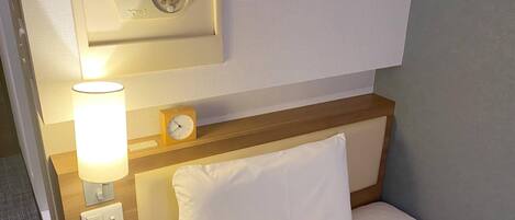 A hotel room with a bed, a nightstand, a lamp, a clock, and a wall-mounted control panel.