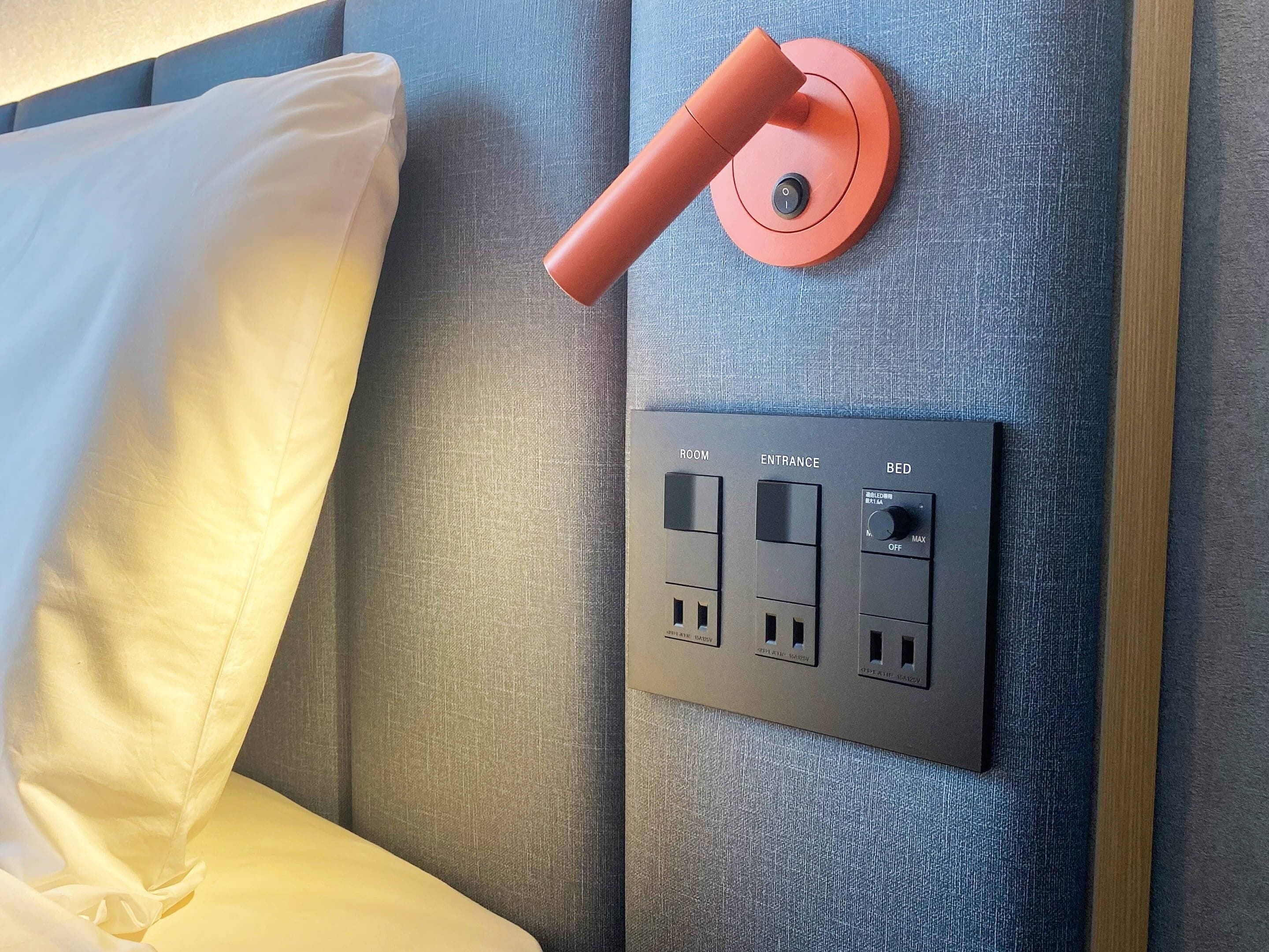 Een bedieningspaneel met labels voor KAMER, INgang en BED, en een stopcontact met stekker.