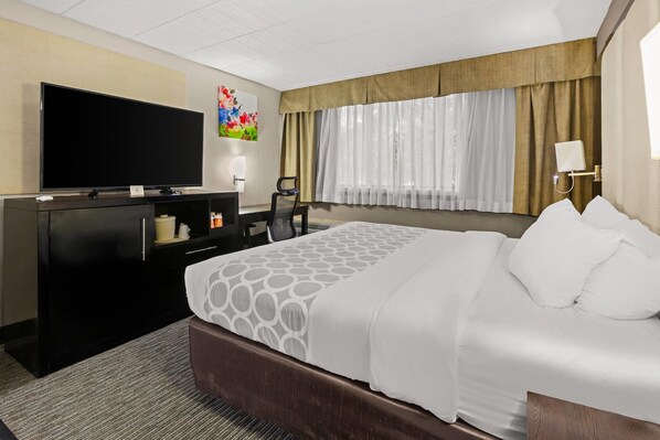 A hotel room with a large bed, a flat-screen TV, a desk with a computer, and a chair. - Suburban Studios Altoona (Altoona)