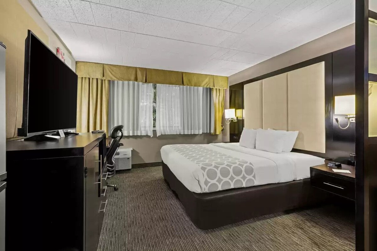 Habitación de hotel con una cama grande, un escritorio con televisión de pantalla plana, una silla y una lámpara de escritorio.