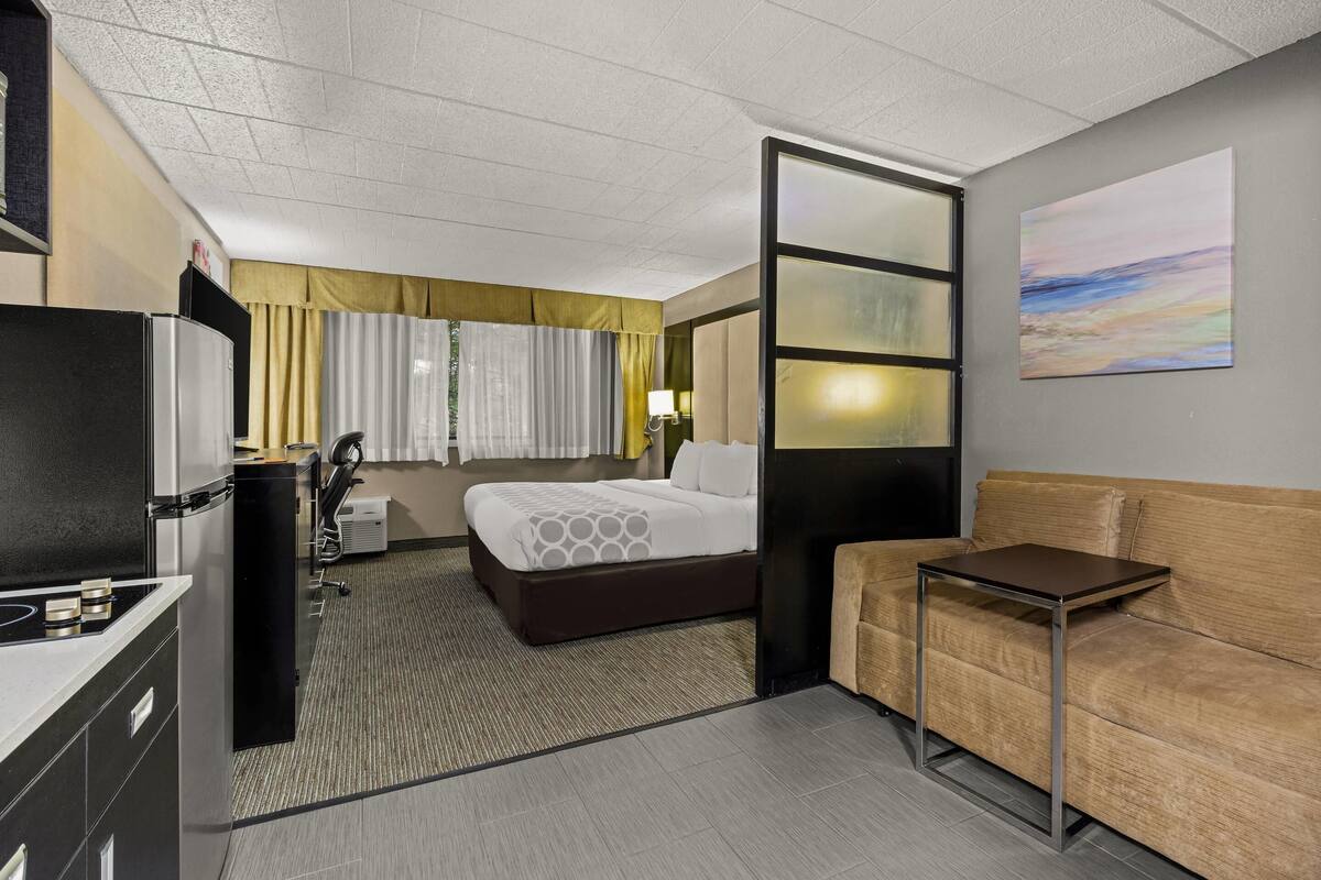 A hotel room with a bed, a sofa, a small table, a desk, a lamp, and a painting on the wall.