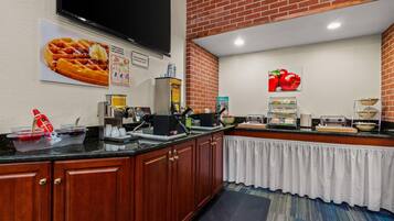 Cozinha de hotel com armários de madeira, bancada preta e parede de tijolos.