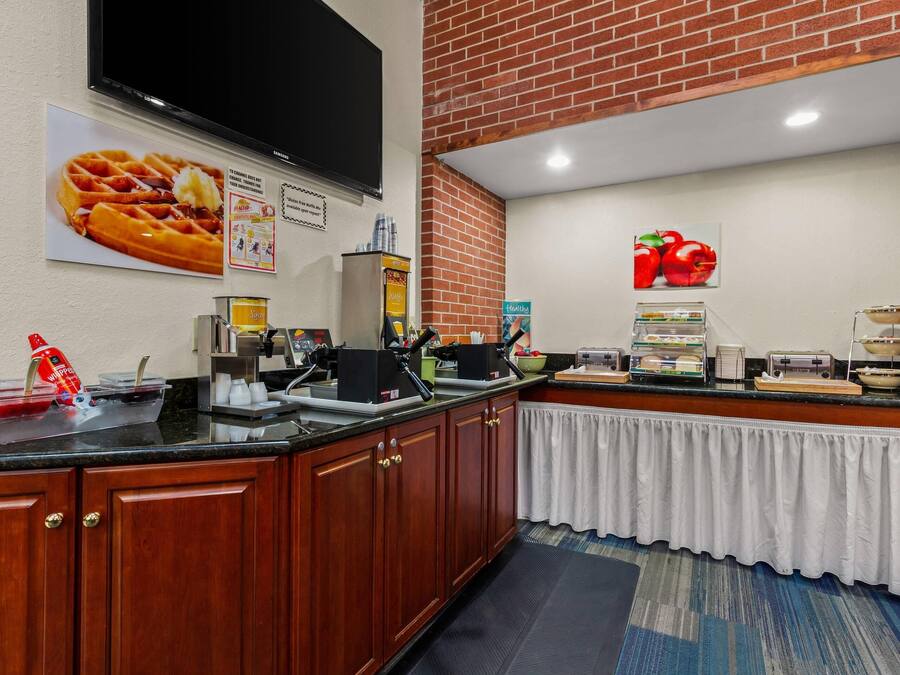 Cozinha de hotel com armários de madeira, bancada preta e parede de tijolos.
