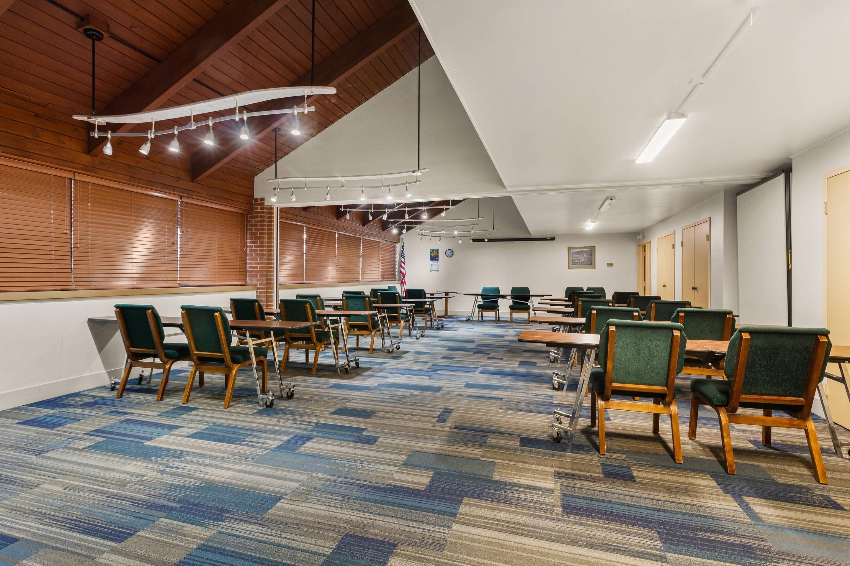 A conference room with tables and chairs, wooden ceiling beams, and a patterned carpet.