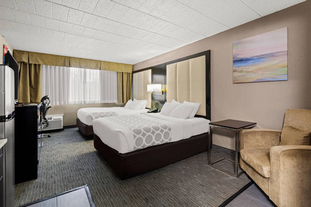 A hotel room with two beds, a desk, a chair, a TV, and a painting on the wall.