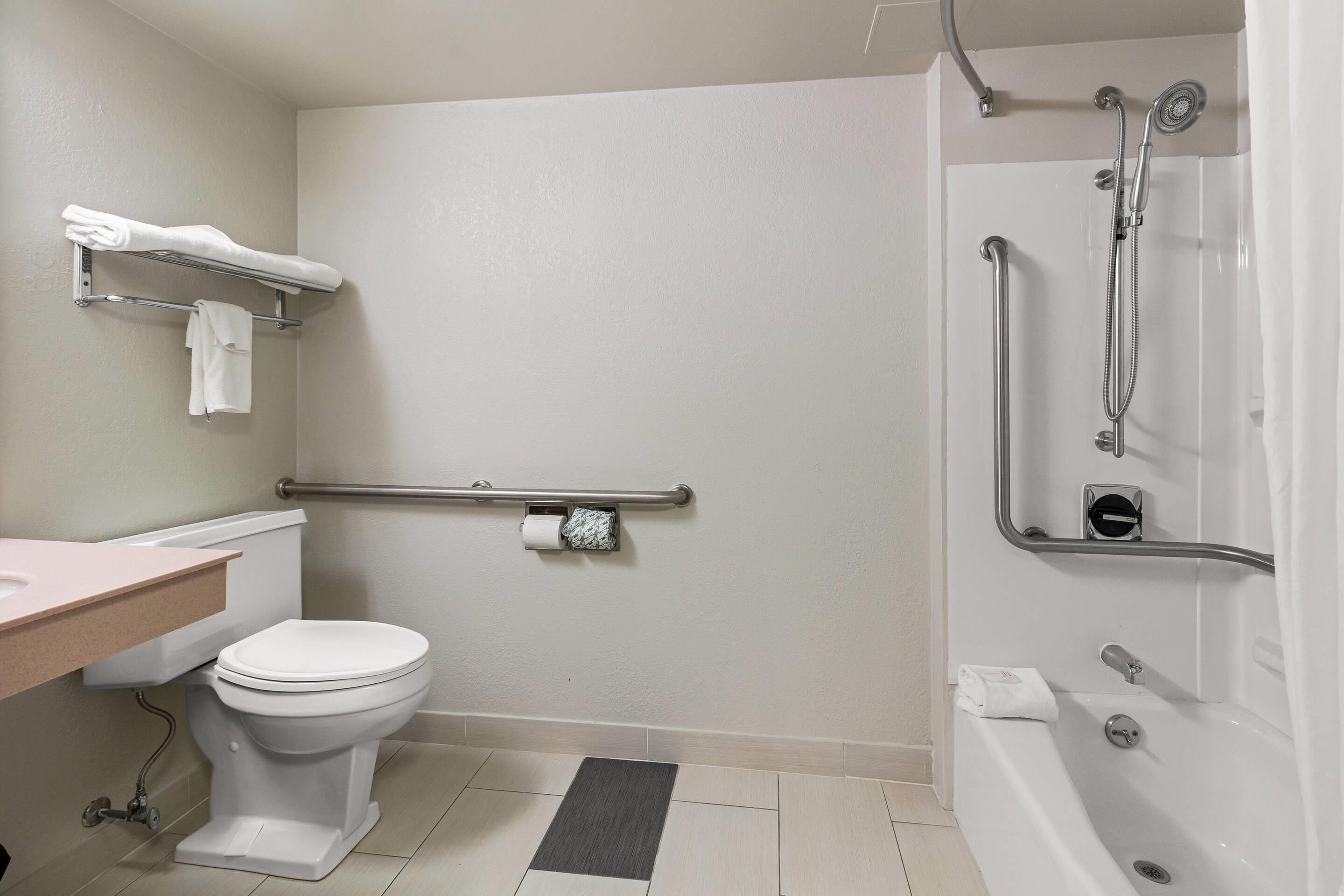 A bathroom with a toilet, sink, shower, and grab bars.