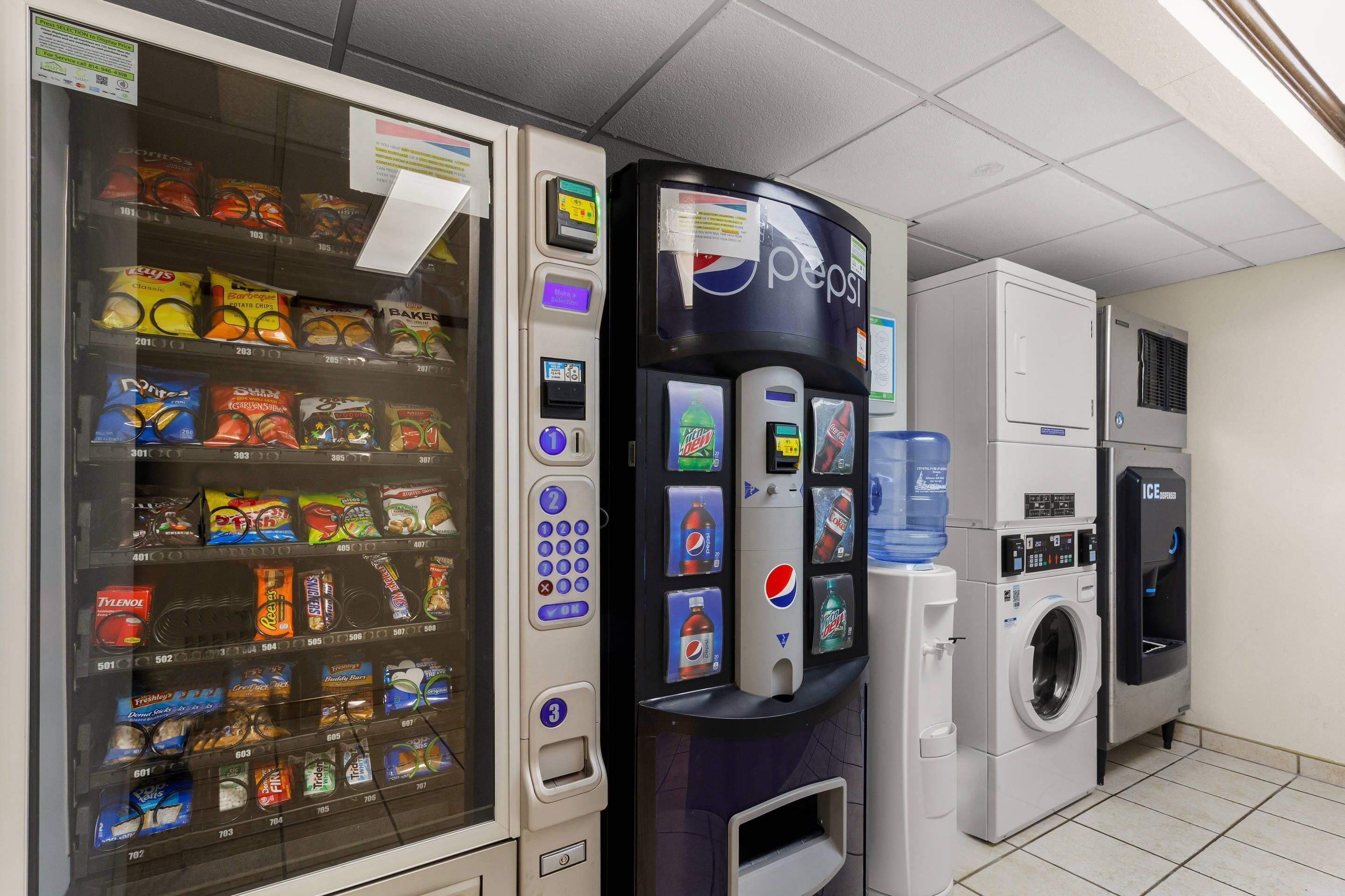 A vending machine with snacks and a Pepsi dispenser, a washing machine, and an ice dispenser in a room with tiled flooring.