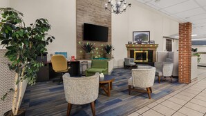 A modern hotel lobby with a flat-screen TV, comfortable seating, a fireplace, and a large plant. - Suburban Studios Altoona (Altoona)