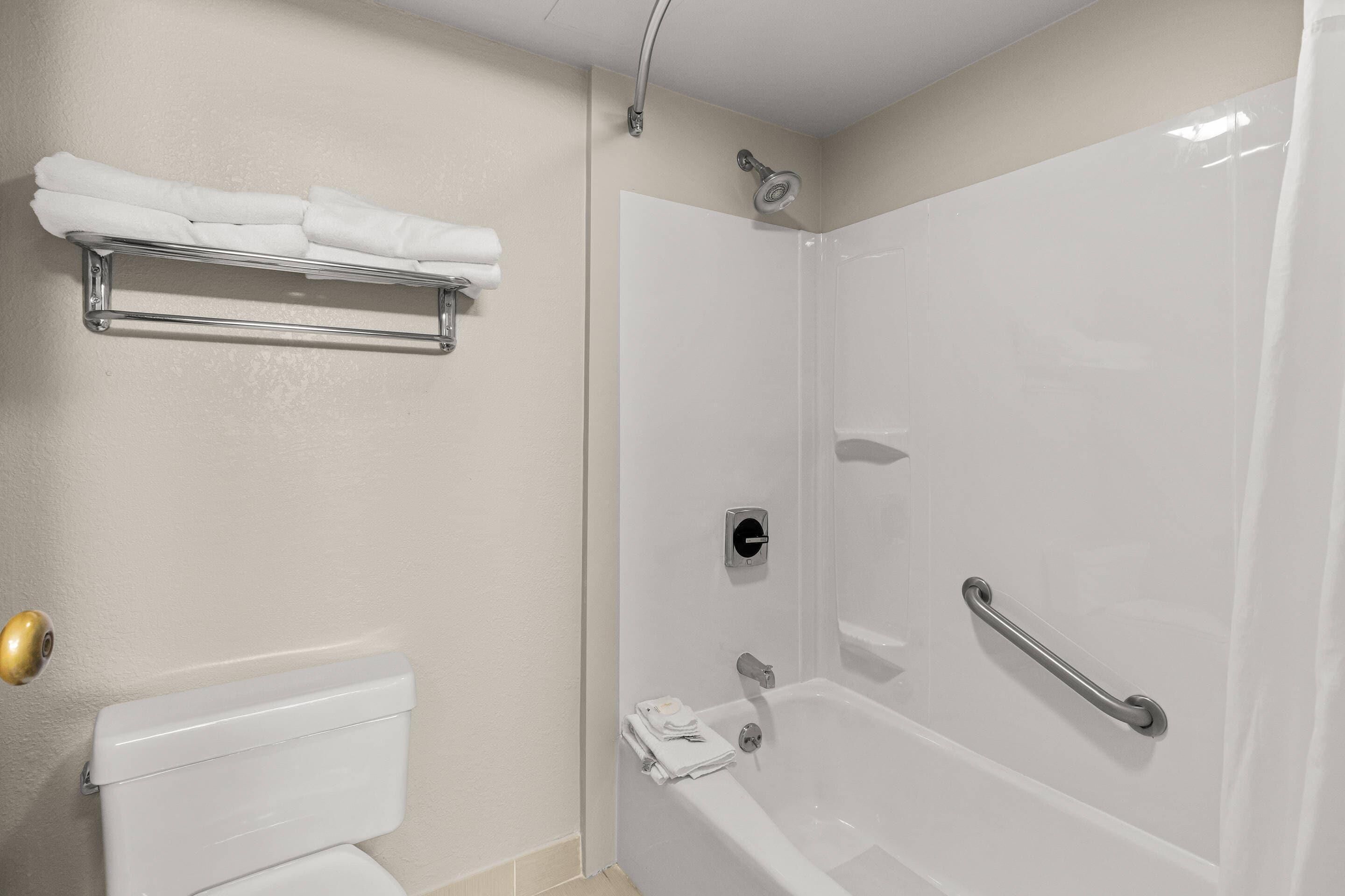 A bathroom with a toilet, a shower with a grab bar, and a towel rack.