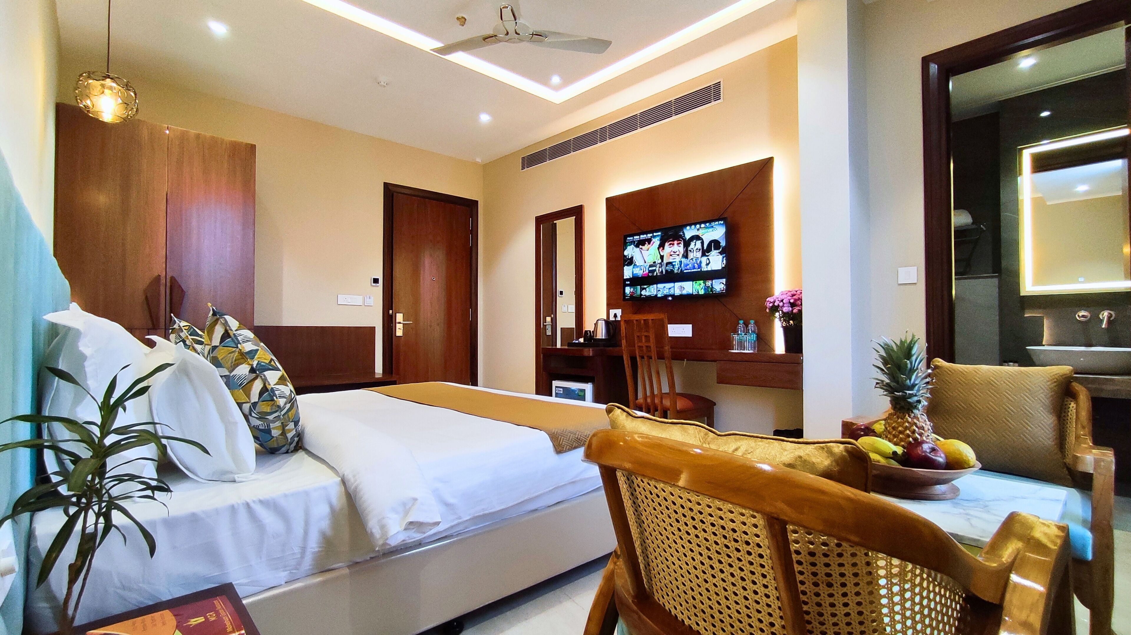 Una habitación de hotel con cama, escritorio, silla, televisión y una planta.