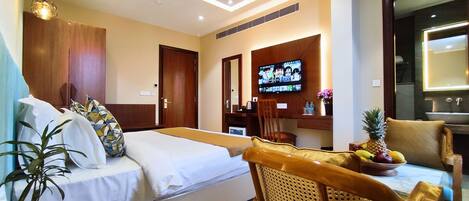 Una habitación de hotel con cama, escritorio, silla, televisión y una planta.